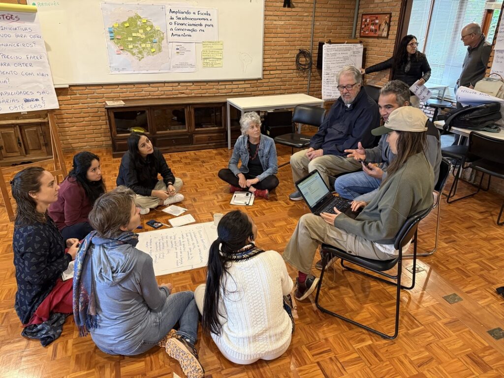 9 workshop participants discussing sitting in a circle having a flipcharts in the middle