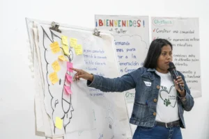 1 workshop participant speaking on the microphone and explaining a flipchart she prepared